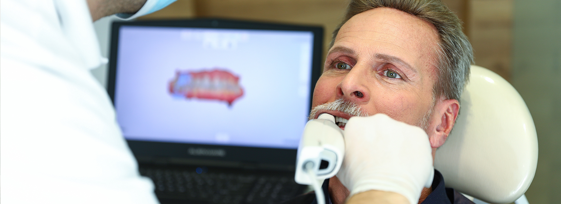 An image of a man receiving dental care, with a dental professional using a computer and various equipment to examine his teeth.